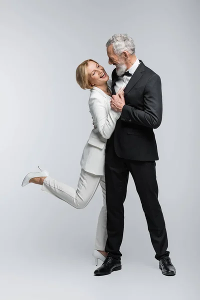 Novia madura positiva abrazando al novio barbudo sobre fondo gris - foto de stock