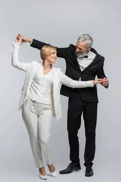 Cheerful bride holding hands of mature groom in formal wear on grey background — Stock Photo