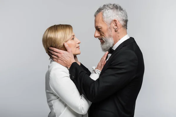 Side view of mature groom in formal wear touching blonde bride isolated on grey — Stock Photo