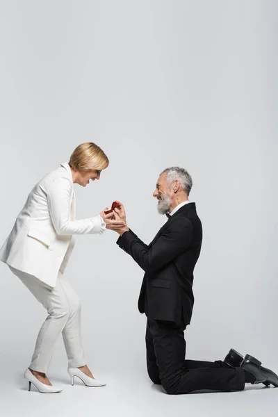 Vista laterale di positivo uomo di mezza età che tiene scatola di gioielli vicino alla donna su sfondo grigio — Foto stock