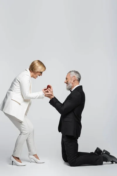 Side view of positive middle aged man holding jewelry box near woman on grey background — Stock Photo