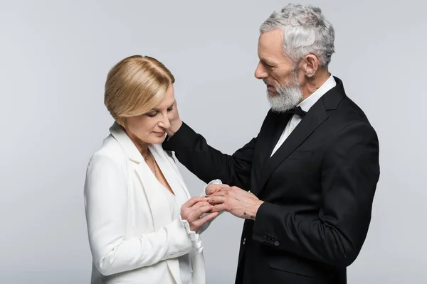 Mature groom touching bride with wedding ring isolated on grey — Stock Photo