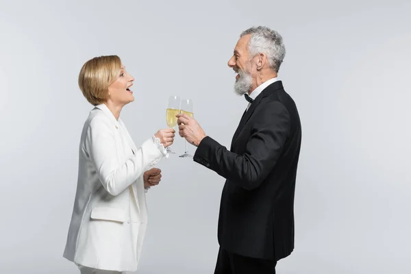 Vista laterale della sposa positiva clinking champagne con lo sposo maturo isolato su grigio — Foto stock