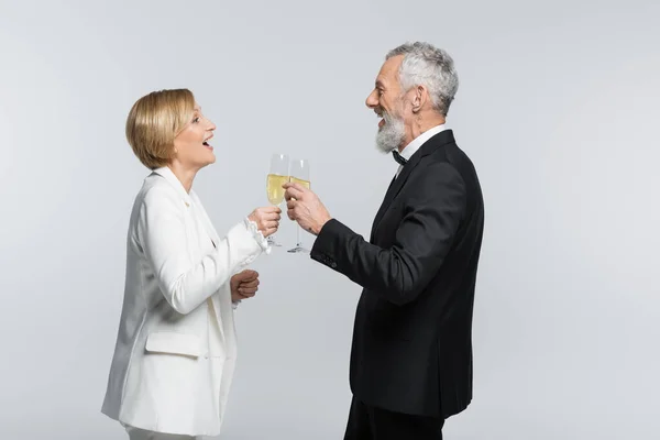 Side view of positive bride clinking champagne with mature groom isolated on grey — Stock Photo