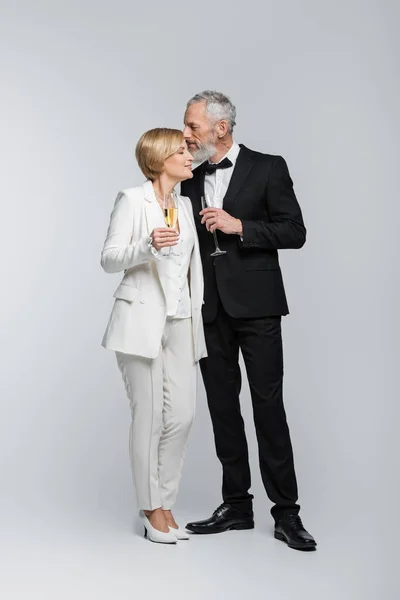 Bräutigam mittleren Alters hält Glas Champagner und küsst Braut auf grauem Hintergrund — Stockfoto