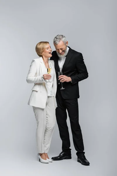 Happy mature bride holding glass of champagne near groom in suit on grey background — Stock Photo