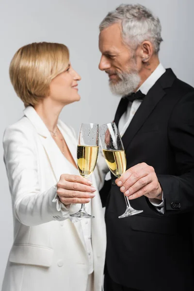 Seitenansicht eines verschwommenen reifen Paares in Hochzeitskleidung, das Champagner auf Grau klirrt — Stockfoto