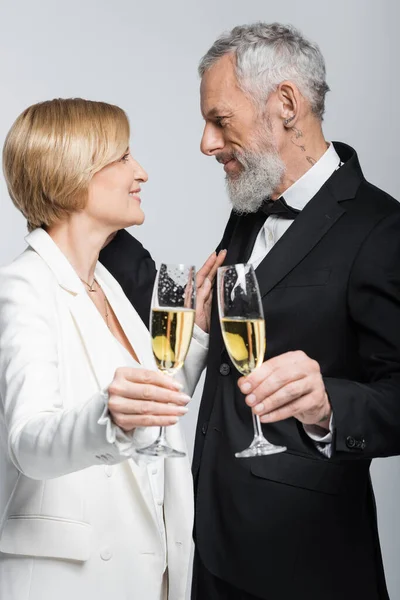 Seitenansicht von glücklichen reifen Frau hält Glas Champagner in der Nähe Bräutigam isoliert auf grau — Stockfoto