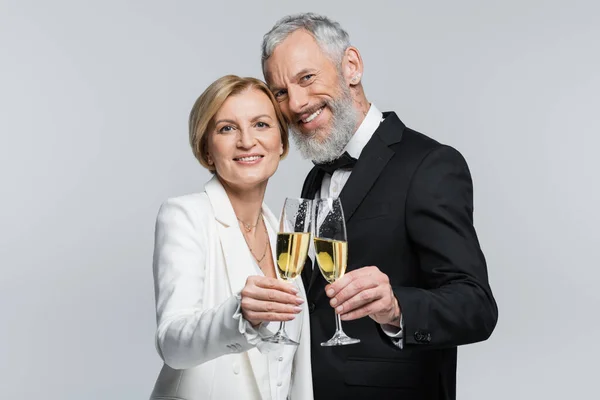 Smiling mature groom looking at camera near bride with champagne isolated on grey — Stock Photo