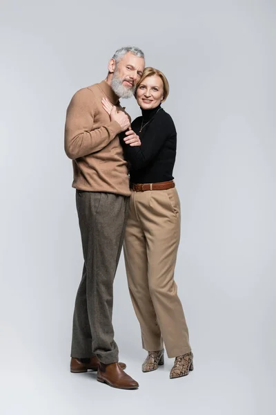 Stylish mature couple looking at camera and hugging on grey background — Stock Photo