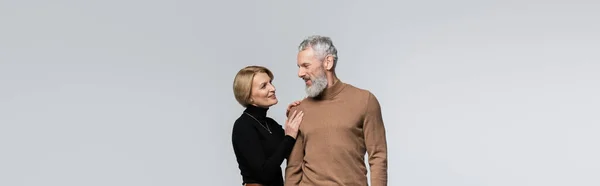 Lächelnde reife Frau berührt bärtigen Ehemann isoliert auf grauem Banner — Stockfoto