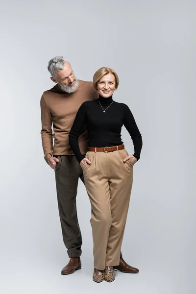 Barbu élégant homme regardant femme blonde souriant à la caméra sur fond gris — Photo de stock