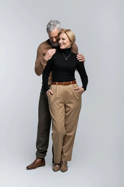 Stilvoller bärtiger Mann umarmt blonde Frau im Rollkragen auf grauem Hintergrund — Stockfoto