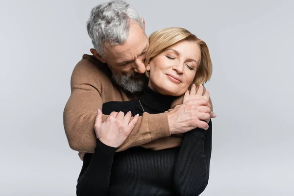 Homme aux cheveux gris embrassant femme avec les yeux fermés isolé sur gris — Photo de stock