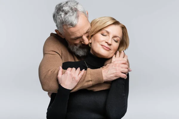 Grey haired man hugging wife with closed eyes isolated on grey — Stock Photo