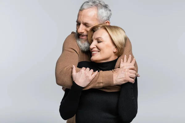 Reifer Mann mit geschlossenen Augen umarmt fröhliche Frau isoliert auf grau — Stockfoto