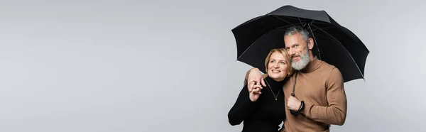 Lächelnder älterer Mann mit Regenschirm und umarmter Frau isoliert auf grauem Banner — Stockfoto