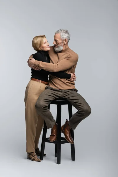 Madura mujer abrazando elegante marido sentado en silla sobre fondo gris - foto de stock