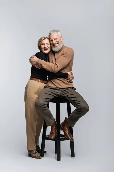 Glückliches und trendiges reifes Paar, das sich umarmt und in die Kamera auf grauem Hintergrund blickt — Stockfoto
