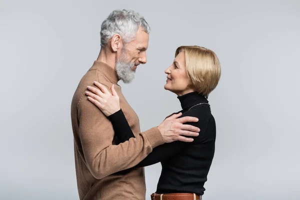 Vista lateral de pareja adulta positiva abrazándose aislada en gris - foto de stock