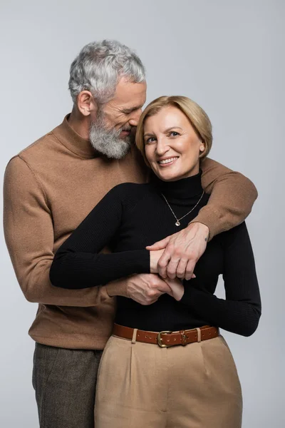 Grey haired man in turtleneck embracing blonde wife isolated on grey — Stock Photo