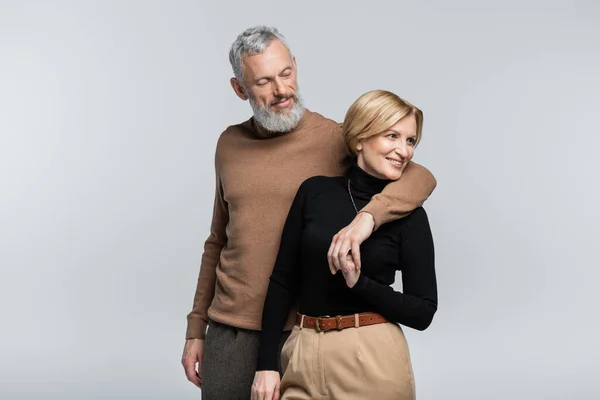 Stilvoller Mann umarmt lächelnde Frau mittleren Alters isoliert auf grau — Stockfoto