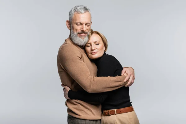 Barbu gris cheveux homme étreignant femme avec les yeux fermés isolé sur gris — Photo de stock