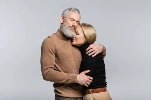 Reifer Mann schließt Augen und umarmt stilvolle Frau isoliert auf grau — Stockfoto