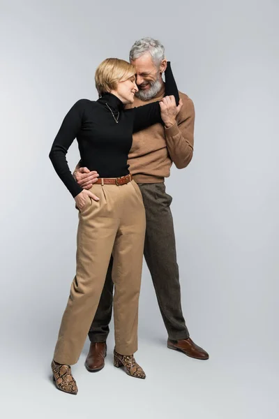 Full length of cheerful mature couple hugging and posing on grey background — Stock Photo