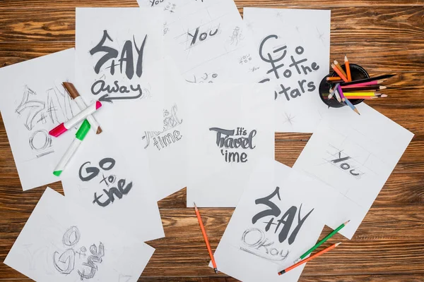 Top view of white paper sheets with various fonts, color pencils and felt pens on wooden surface — Stock Photo