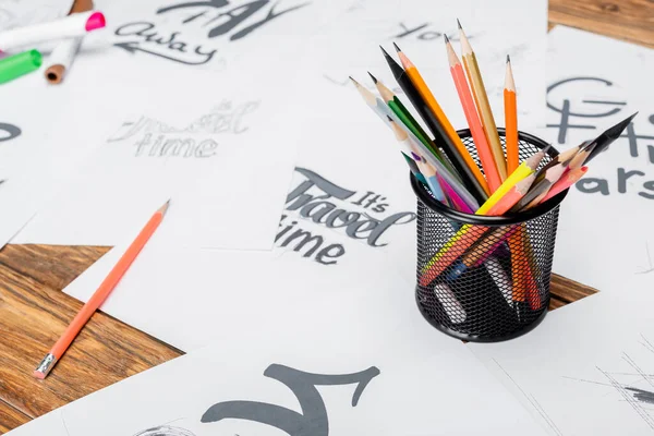 Color pencils near blurred papers with various fonts on wooden desk — Stock Photo