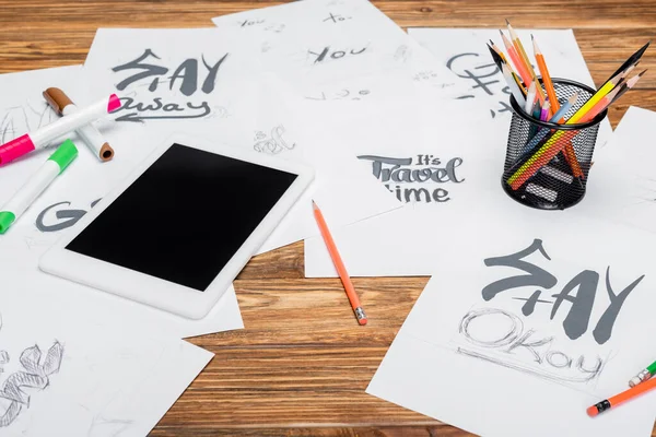 Digital tablet with blank screen, color pencils and papers with different fonts on wooden desk — Stock Photo