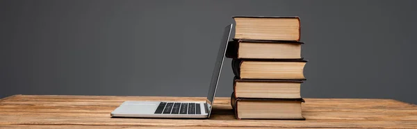 Stack of books and laptop on wooden desk isolated on grey, banner — Stock Photo