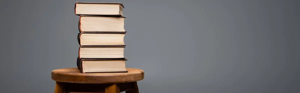 Books stacked on wooden stool isolated on grey with copy space, banner — Stock Photo