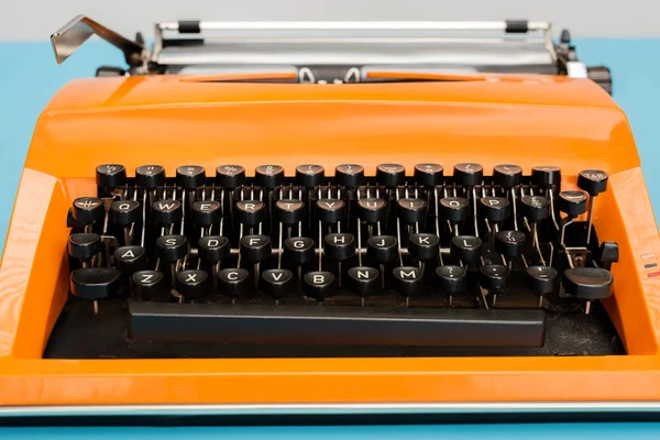 Close up view of bright orange typewriter with black keyboard isolated on blue — Stock Photo