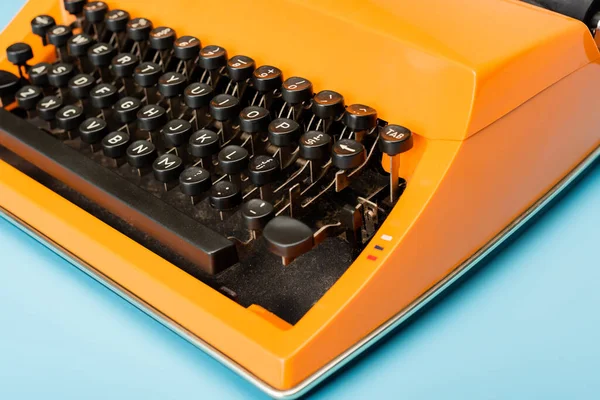 Nahaufnahme der schwarzen Tastatur einer orangefarbenen Schreibmaschine auf blauem Hintergrund — Stockfoto