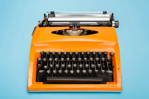 Bright orange typewriter with black keyboard on blue background — Stock Photo