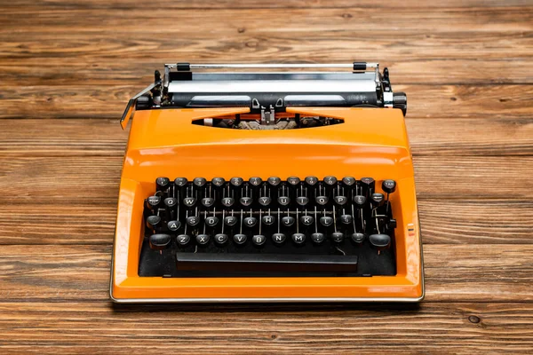 Bright orange typewriter with black keyboard on textured wooden surface — Stock Photo