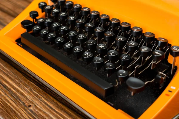 Close up view of black keyboard of orange typewriter on wooden surface — Stock Photo