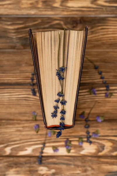 Draufsicht auf getrocknete Lavendelblüten und Buch auf verschwommenem Holztisch — Stockfoto