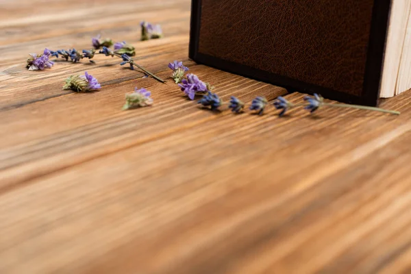 Buch und getrocknete Lavendelblüten auf verschwommener Holzoberfläche — Stockfoto