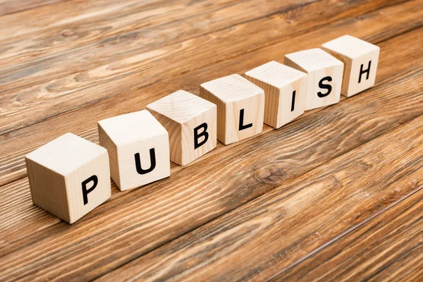 Row of wooden cubes with publish lettering on brown textured surface — Stock Photo