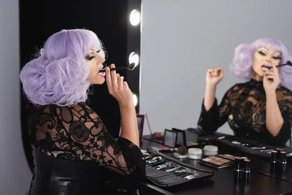 Excêntrico drag queen sentado com escova cosmética perto do espelho — Fotografia de Stock