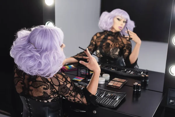 Drag queen em peruca roxa olhando para a reflexão turva no espelho — Fotografia de Stock