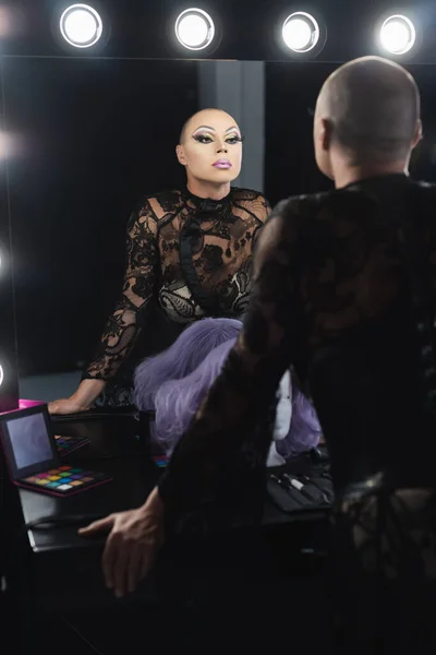 Man in black lace dress and spectacular makeup looking in mirror in dressing room — Stock Photo