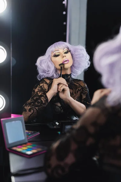 Drag queen in violet wig applying face powder near mirror — Stock Photo