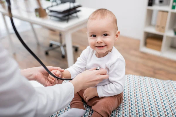 Doctor in while coat examining smiling baby boy with stethoscope in hospital — Stock Photo