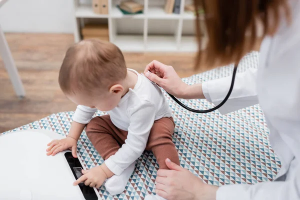 Medico di famiglia che esamina il bambino con stetoscopio vicino alla scala elettronica in clinica — Foto stock