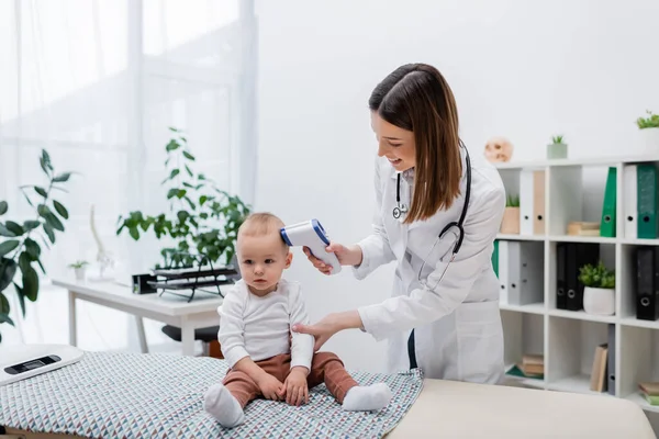Positiver Hausarzt überprüft Temperatur von Säugling mit Pyrometer in Klinik — Stockfoto