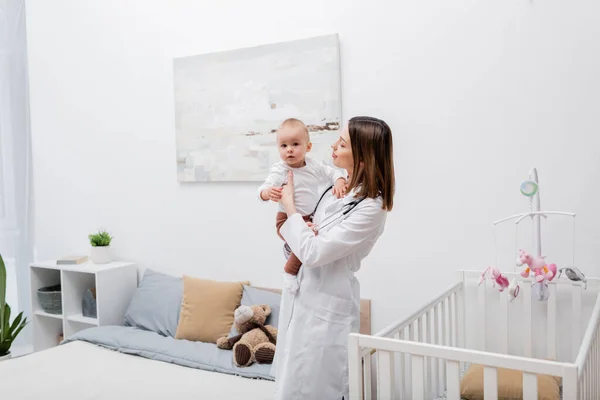 Médecin de famille tenant bébé garçon près de la crèche dans la chambre — Photo de stock